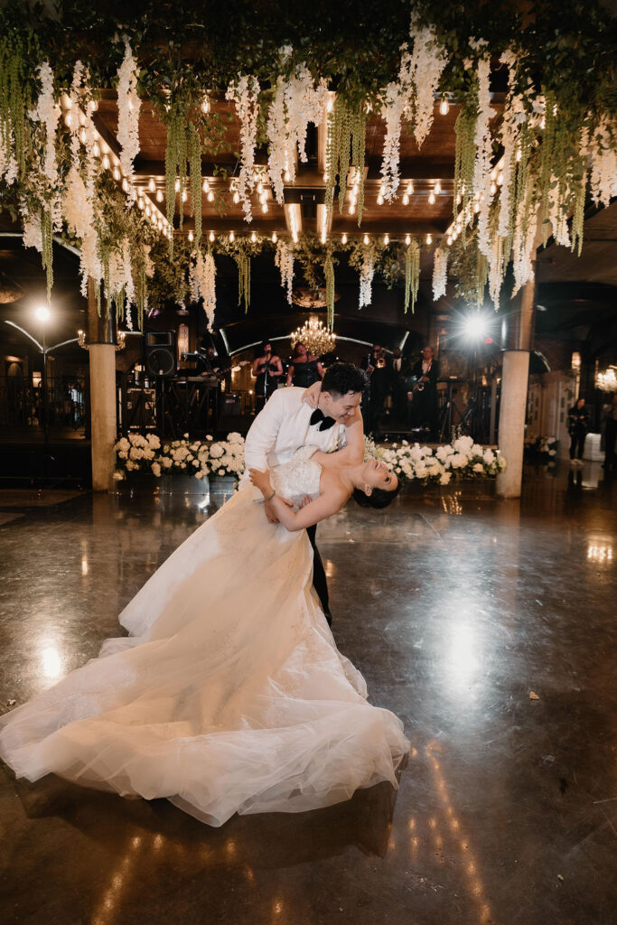 Bride and groom sharing their first dance at The Astorian wedding venue in Houston beneath floral ceiling installations and chandelier lighting