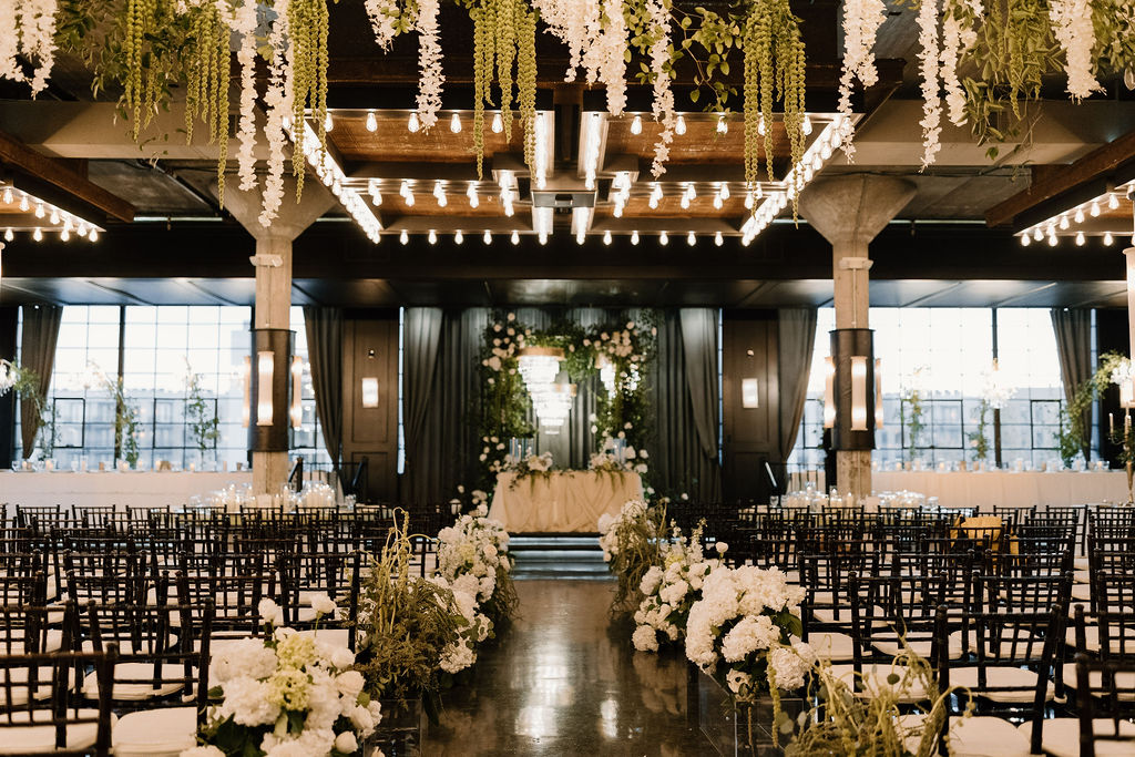 A wide-angle view of a custom ceremony space with layered florals, sculptural lighting, and refined architectural detail, capturing the scale of luxury wedding planning