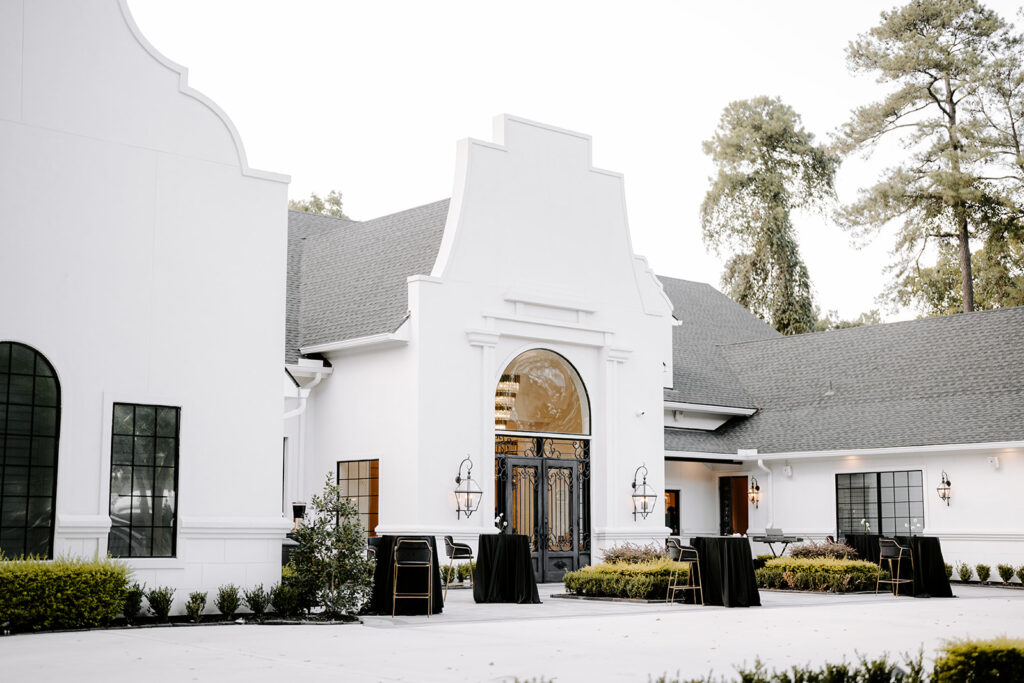 Exterior of a modern white wedding venue with black accents and cocktail tables set for a formal event