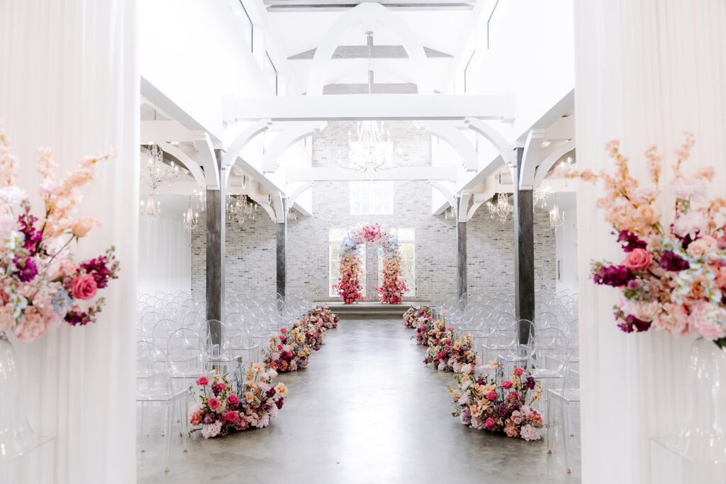 Ceremony aisle in a light-filled venue, lined with vibrant floral arrangements leading to a modern floral arch