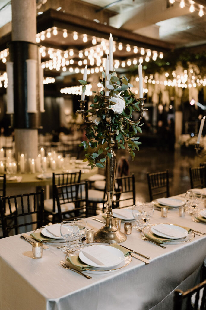 Gold candelabra centerpiece with floral accents on a reception table.