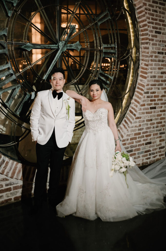 Bride and groom standing in front of the large brass clock wall at The Astorian wedding venue in Houston