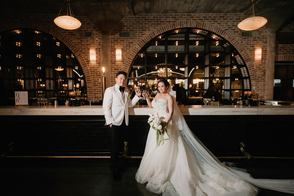 Bride and groom standing in front of the built-in bar at The Astorian wedding venue in Houston with brick arches and warm lighting